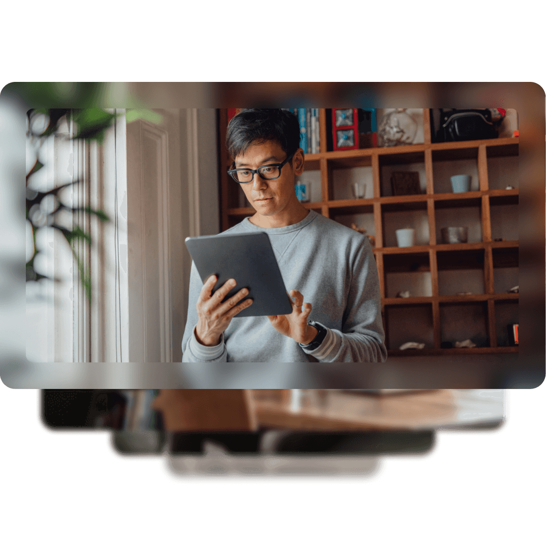 A man standing using his tablet while standing in front of a bookcase.