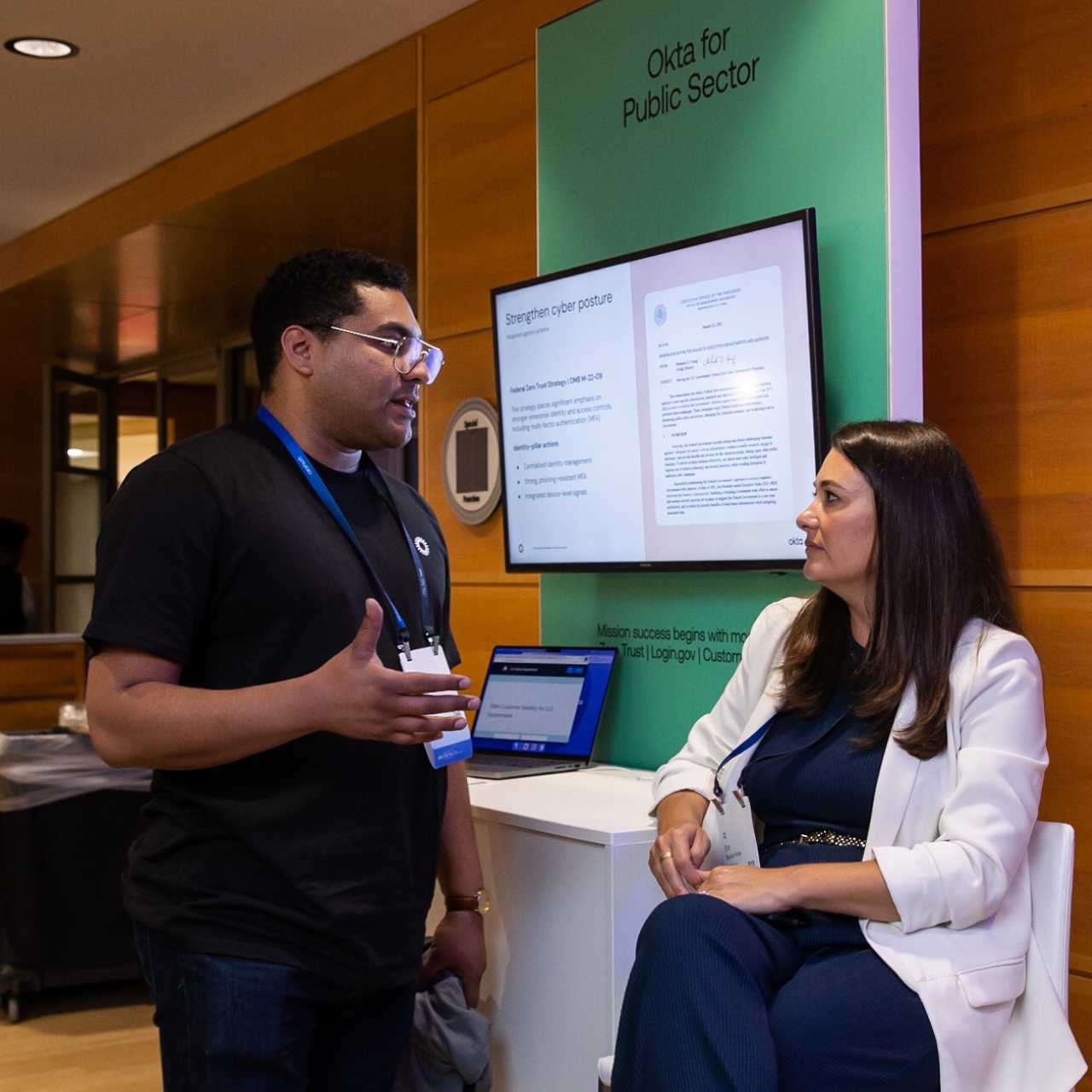 Man and woman talking at Okta for Public Sector booth at Oktane