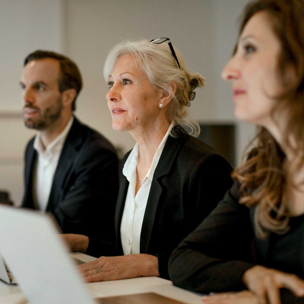 One man and two female colleagues sitting at a table with laptops out. 