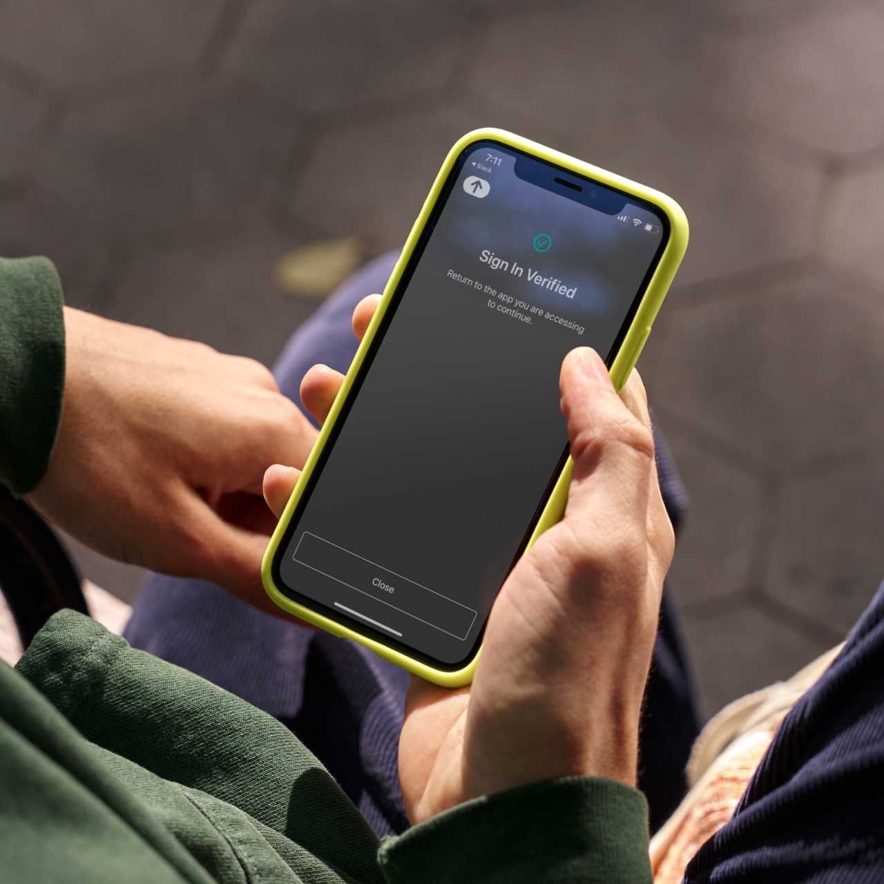 Image of a hand holding a smartphone in a yellow case that shows an Okta Verify notification. 