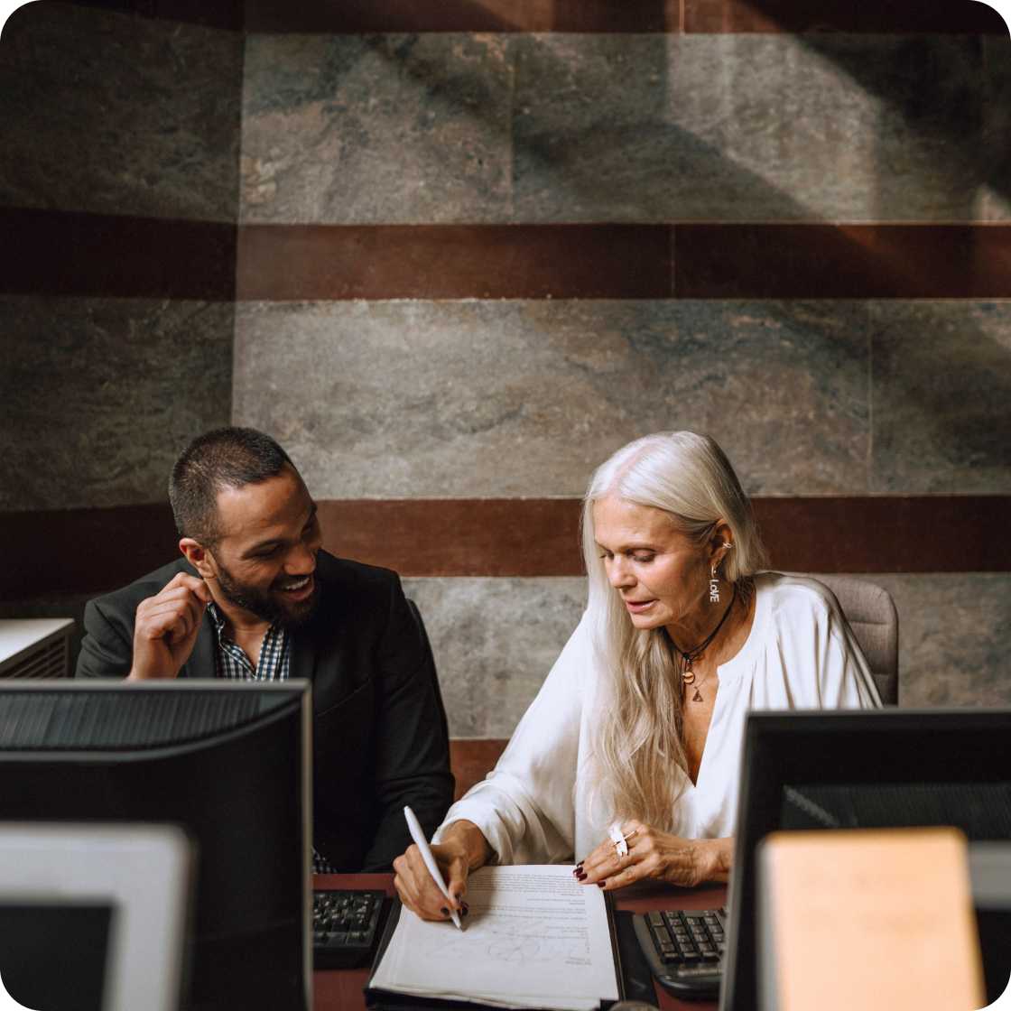 Man and woman sitting at desks while reviewing paper documents. 