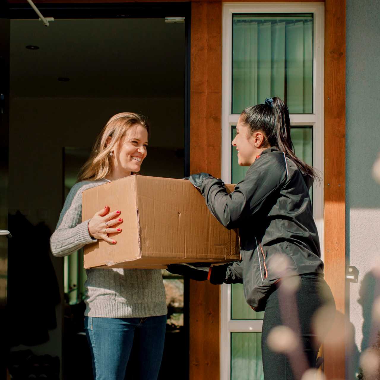 Lieferdienst-Mitarbeiterin, die einer Frau ein Paket aushändigt.