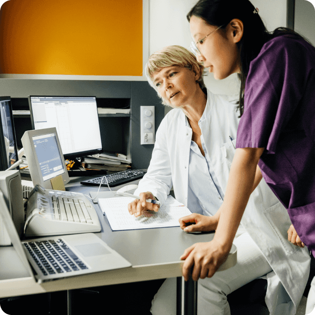 Women in healthcare setting lean over computers discussing test results