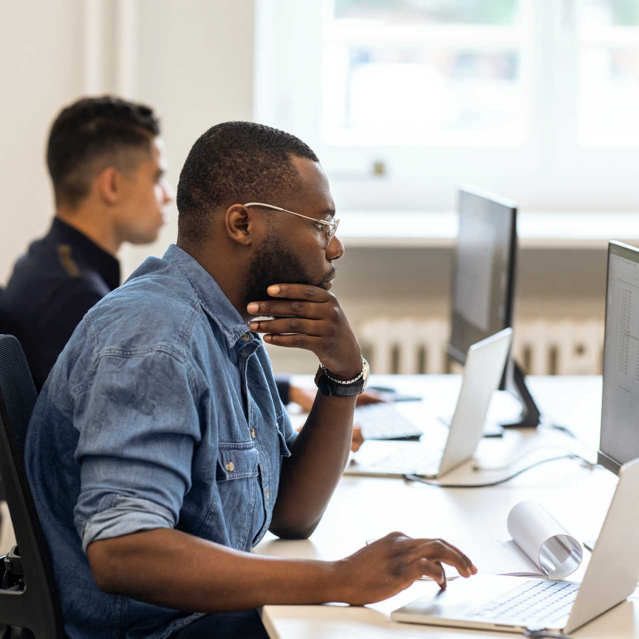 A man working on his computer next to a coworker in the office.