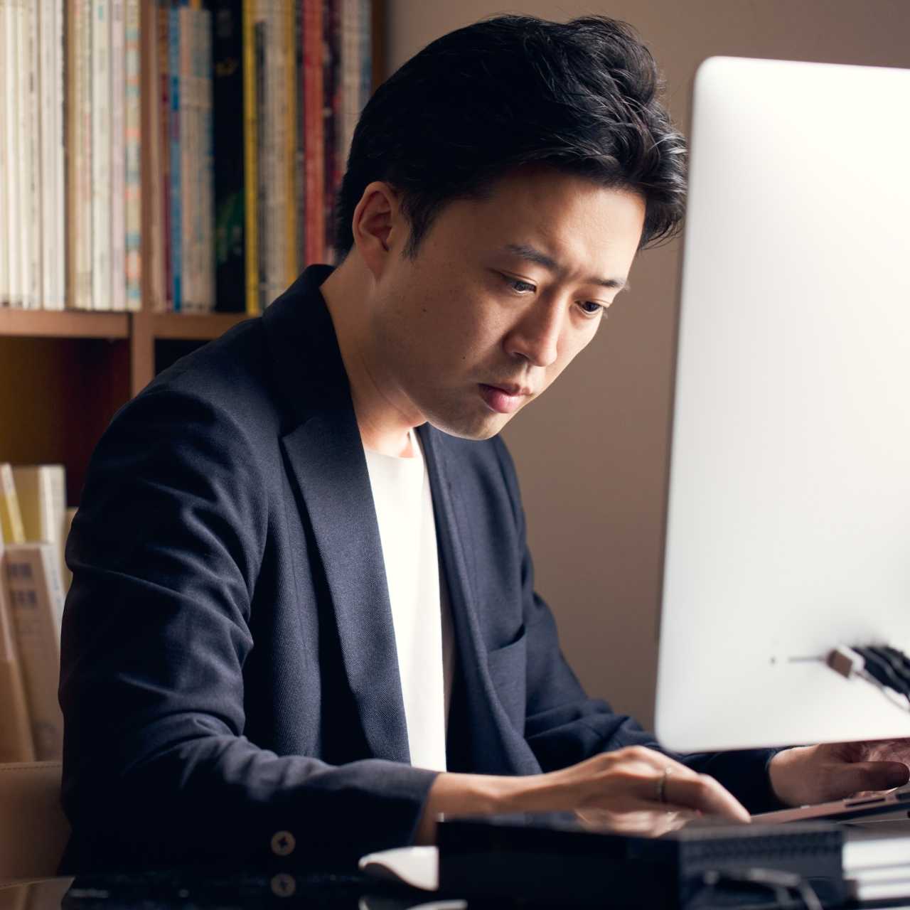 Man in white shirt and blue blazer looking down and typing on desktop computer