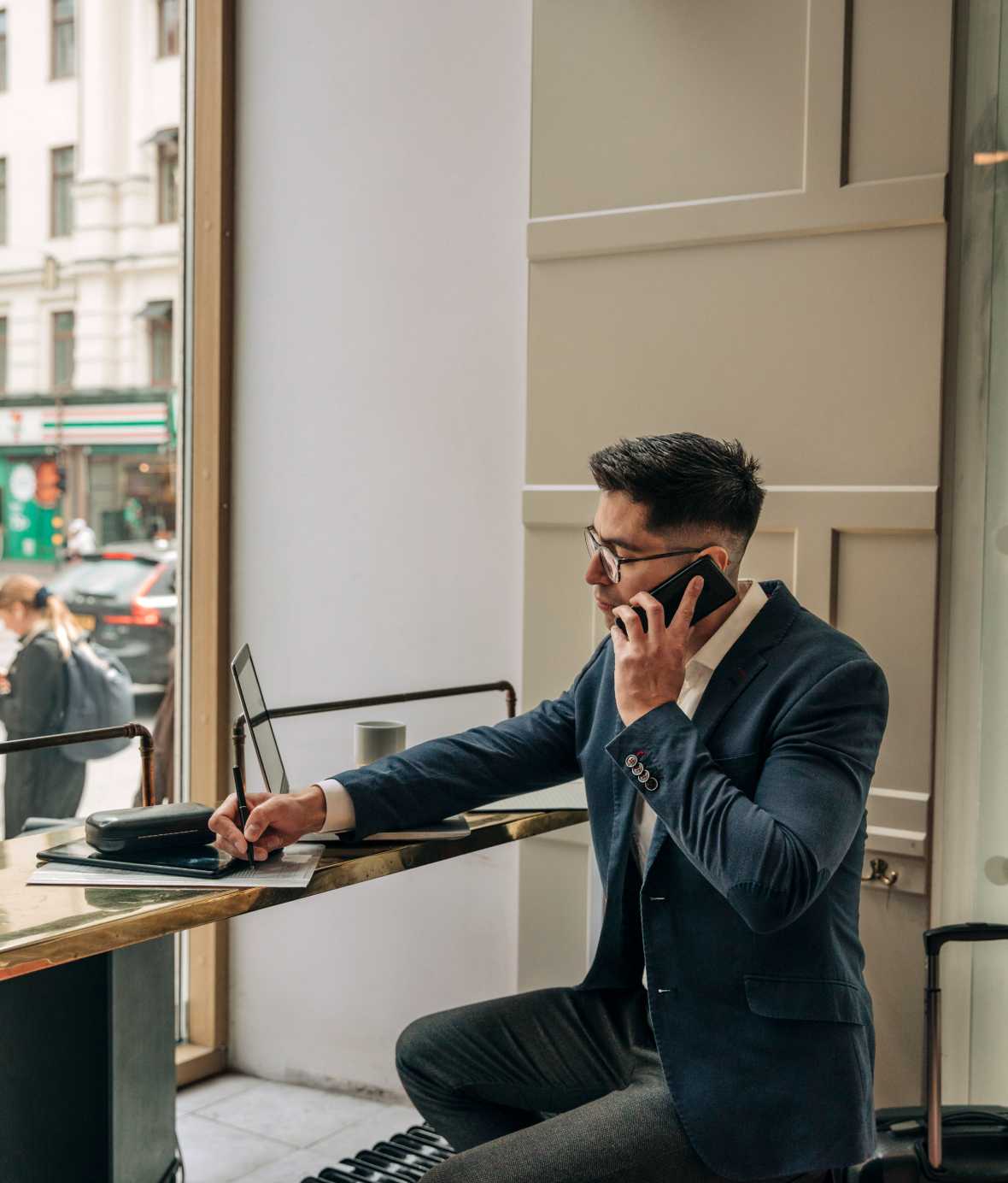 Image of man in suit and tie standing in front of granite and wood striped wall talking on smartphone with mug in hand