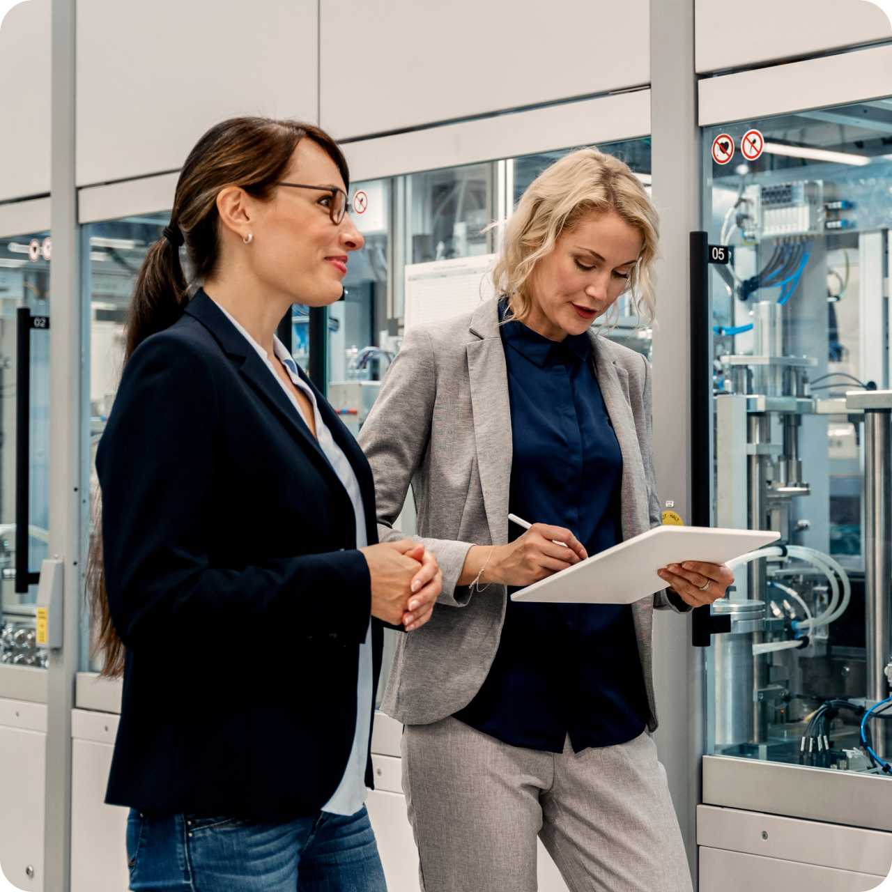  A woman taking notes and her coworker walk beside each other past a factory room.