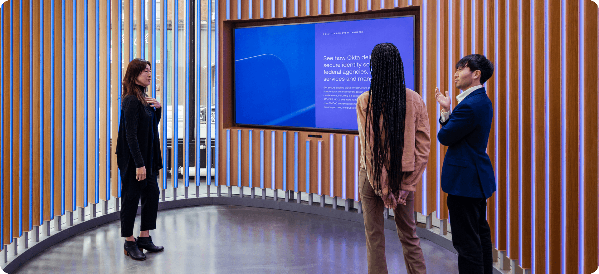 Image of two woman and one man chatting in front of TV at booth at Oktane