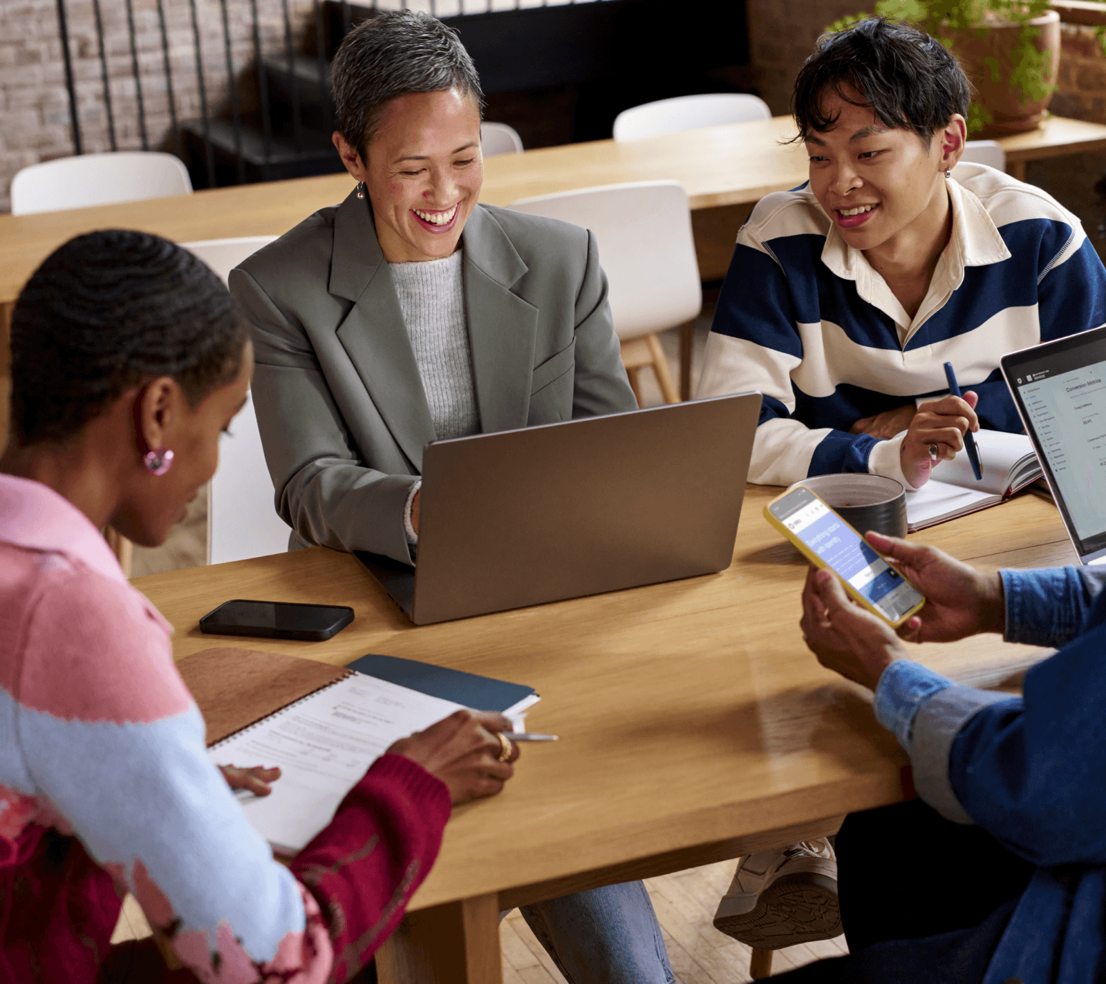 Bild mit lächelnden Arbeitskollegen, die mit Laptop, Smartphones und Notizblöcken in den Händen an einem Besprechungstisch sitzen.