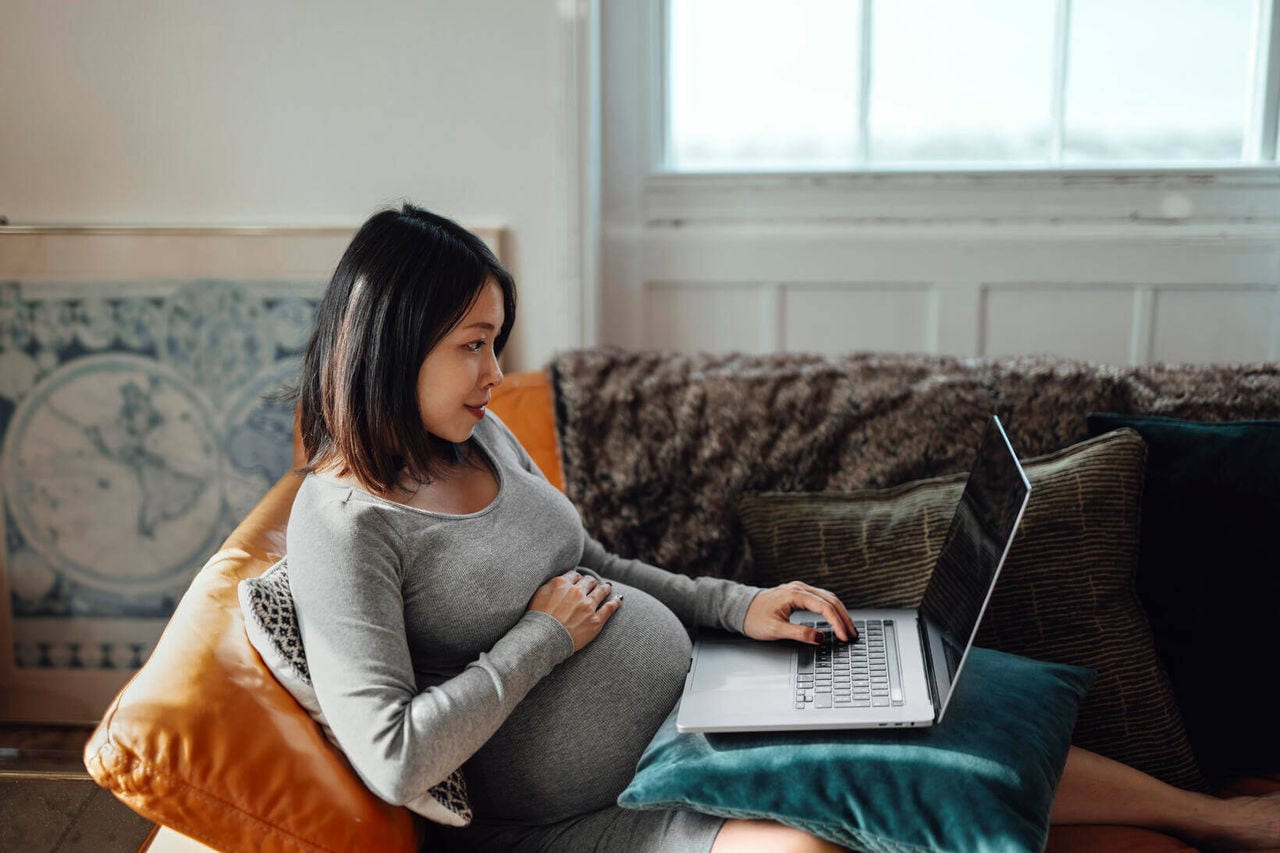 pregnant woman lies on the sofa with a laptop on her lap