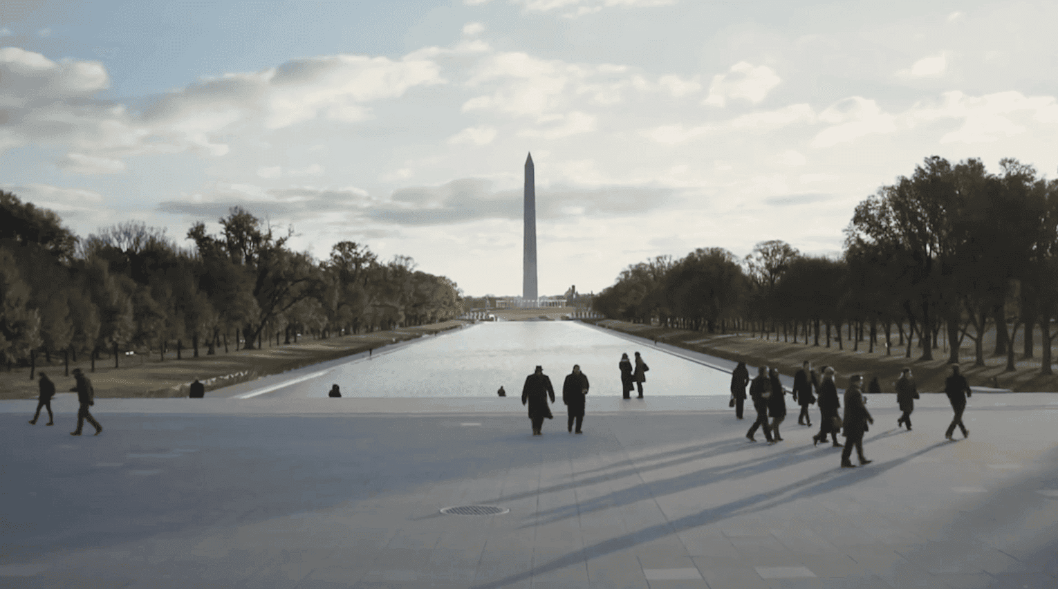 Image of people walking through a small square with an obelisk.