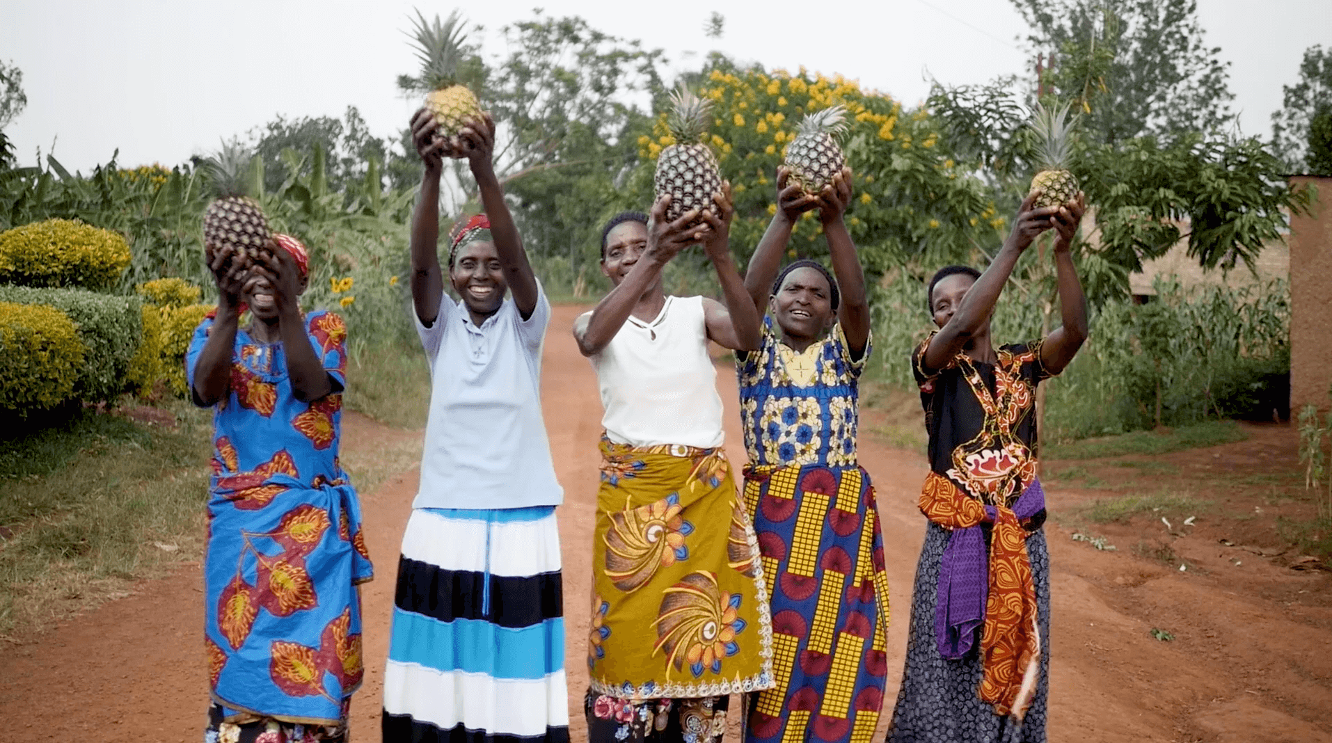 Five happy women smiling at the camera while carrying a pineapple in their hands.