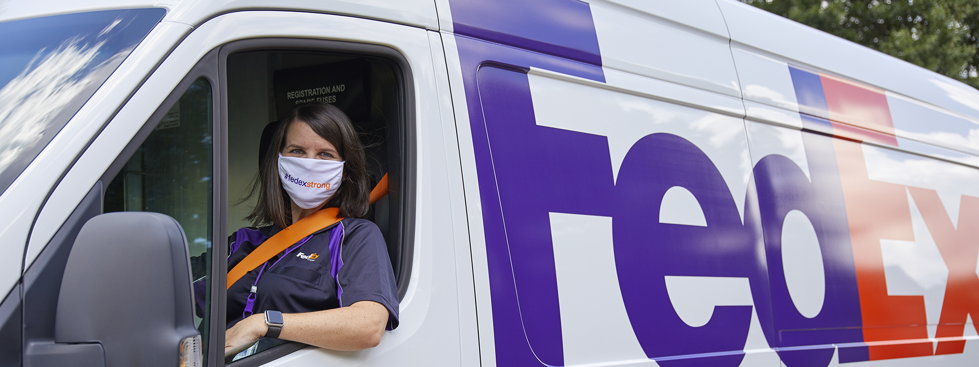 Woman in driver's seat of FedEx van, wearing a mask.