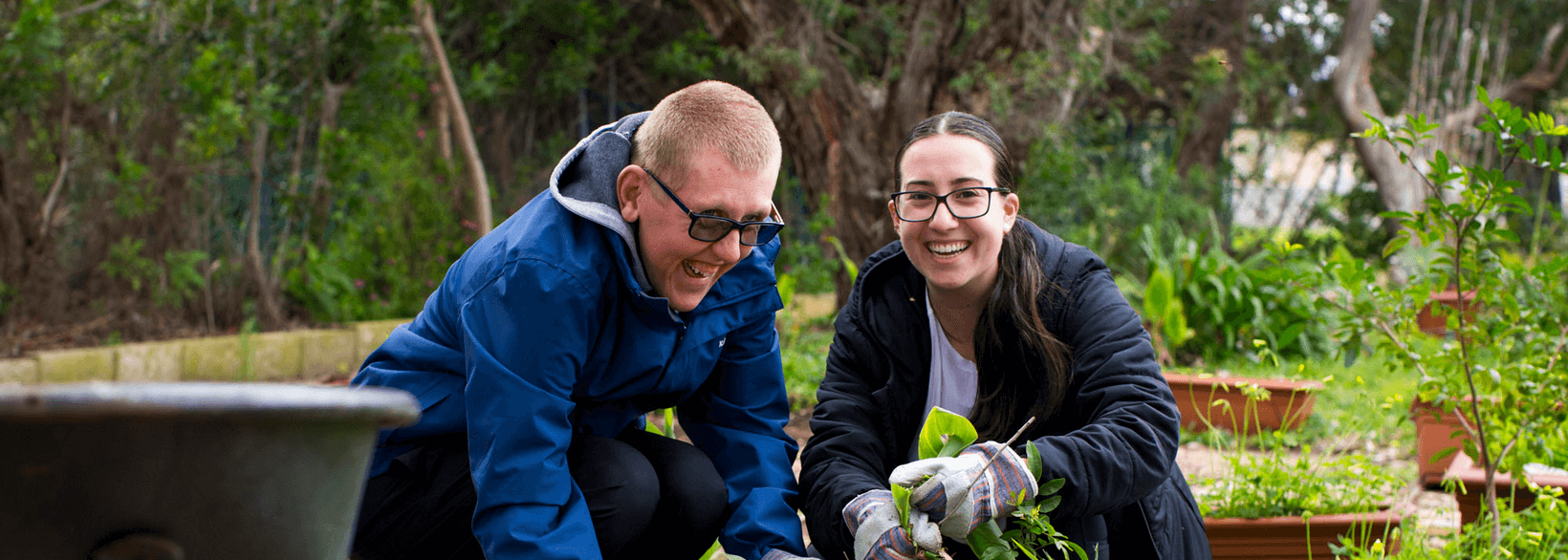 Image of two persons smiling at the camera while planting.