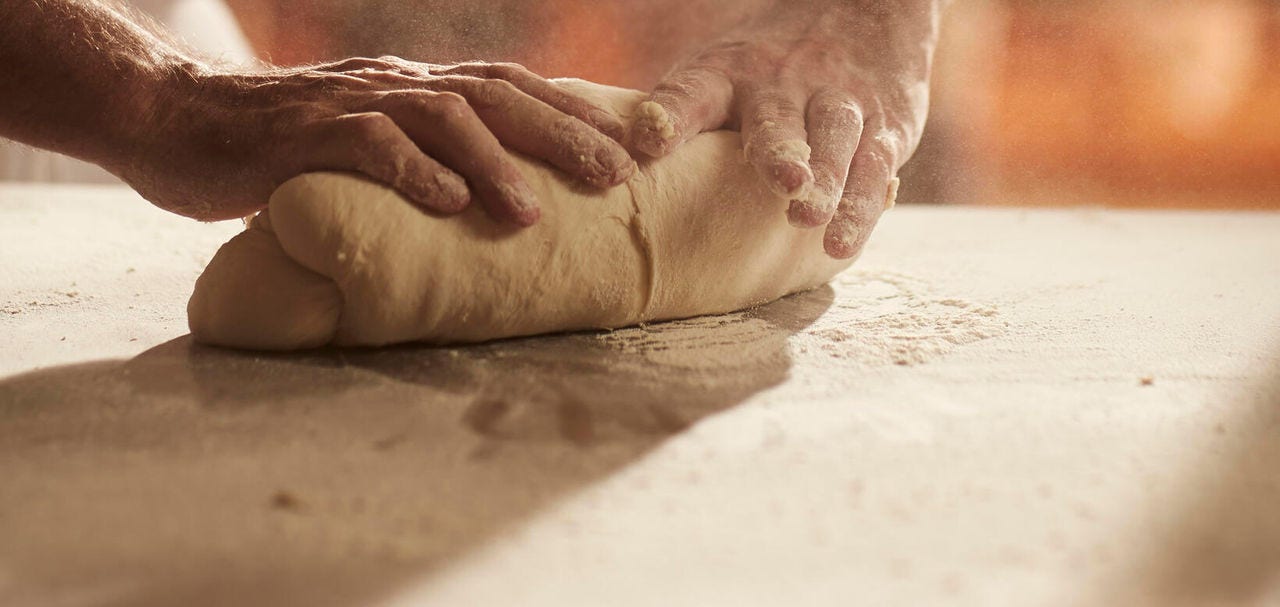 A pair of hands working with baking dough on a board.