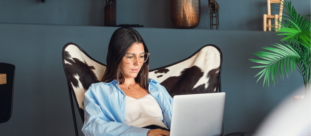 Image of a woman sitting on a chair in a common space while working on a laptop.